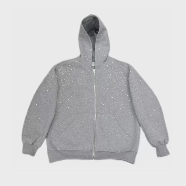 May include: A gray zip-up hoodie with a hood and front pockets. The hoodie is covered in small, scattered white embellishments. The zipper is silver. The cuffs and waistband are ribbed.