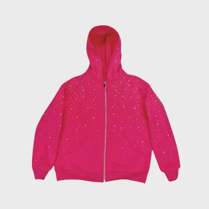 May include: A vibrant fuchsia zip-up hoodie with a hood and front pockets. The hoodie is adorned with a pattern of small, white, sparkling embellishments. The zipper is silver. The garment is made of a soft material.