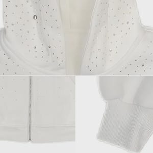May include: A white hooded sweatshirt with a silver zipper and numerous small, sparkling embellishments. The cuffs and hood lining are ribbed. The overall design is clean and minimalist, with a focus on the decorative elements.