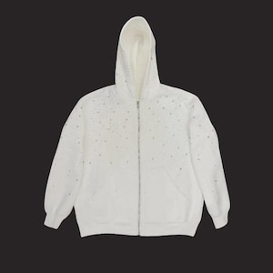 May include: White zip-up hoodie with a drawstring hood and front pockets. The hoodie is embellished with scattered silver-colored rhinestones. The zipper is silver-colored. The hoodie is made of a soft material.