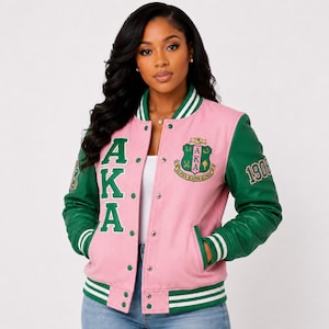May include: A pink and green varsity jacket featuring the letters AKA in large green font on the right side, the number 1908 on the left sleeve, and an embroidered crest on the left chest with the text Alpha Kappa Alpha inside.