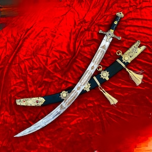 Op de afbeelding: Een gebogen zwaard met een patroonstalen lemmet met gegraveerd Arabisch schrift, een donker handvat met goudkleurige accenten en een zwarte schede versierd met ingewikkelde goudkleurige metalen fittingen, bloemmotieven, rode stenen en twee hangende kwastjes.