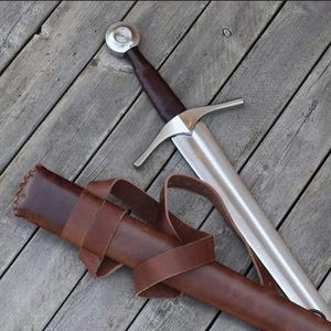 May include: A medieval sword with a polished steel blade and a brown leather-wrapped handle. The sword features a crossguard and a circular pommel. A brown leather sheath with a belt is also present.