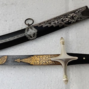 May include: An ornate sabre with a black handle and scabbard. The blade is silver with gold accents. The scabbard is decorated with silver floral designs and ring attachments. The hilt is silver.