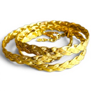 May include: A gold-colored braided belt with a clasp closure. The belt is made of a shiny, metallic material and is arranged in a circular pattern. The braided design adds texture and visual interest to the accessory.