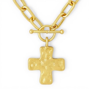 May include: A gold-colored necklace with a cross pendant. The necklace features a toggle clasp and a textured cross charm. The chain links are large and rectangular. The jewelry is set against a white background.