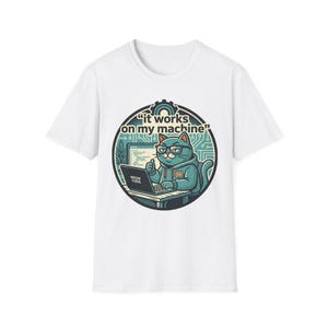 Può includere: T-shirt bianca con un gatto dei cartoni animati con occhiali e una felpa con cappuccio, che lavora su un laptop. Il design include il testo "it works on my machine" e "MEOW CODE". Il gatto fa il pollice in su.