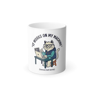May include: White ceramic mug with a cartoon cat wearing glasses and a hoodie, working on a laptop. The mug has the text "IT WORKS ON MY MACHINE" and "(famous last words)" in black font. The cat is sitting at a small desk with a coffee cup.