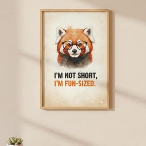 Pode incluir: Uma impressão emoldurada com uma ilustração em aquarela de um panda-vermelho usando óculos. O texto diz: «I'M NOT SHORT, I'M FUN-SIZED». A obra de arte tem uma estética quente e vintage, com um fundo marrom claro e uma moldura de madeira. A impressão é exibida em uma parede clara.