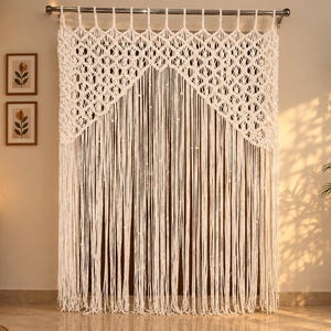 May include: A cream-colored macrame curtain featuring an intricate knotted diamond pattern at the top section, transitioning into long, straight, vertical fringe strands that hang down to create a textured, layered appearance on a metal rod.