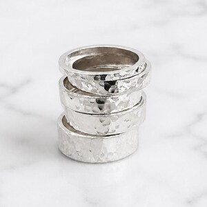 Könnte beinhalten: Ein Stapel von vier silbernen Ringen mit gehämmerten Texturen. Die Ringe sind unterschiedlich breit, wobei der oberste Ring der dünnste und der unterste Ring der dickste ist. Die Ringe sind übereinander gestapelt.
