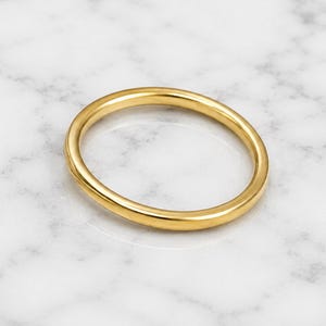 Könnte beinhalten: Ein schlichter, polierter Goldring mit einer glatten, abgerundeten Oberfläche und einer durchgehenden Kreisform. Das Metall hat ein reflektierendes, hochglänzendes Finish, das das Licht einfängt und ein sauberes, einheitliches Erscheinungsbild erzeugt.