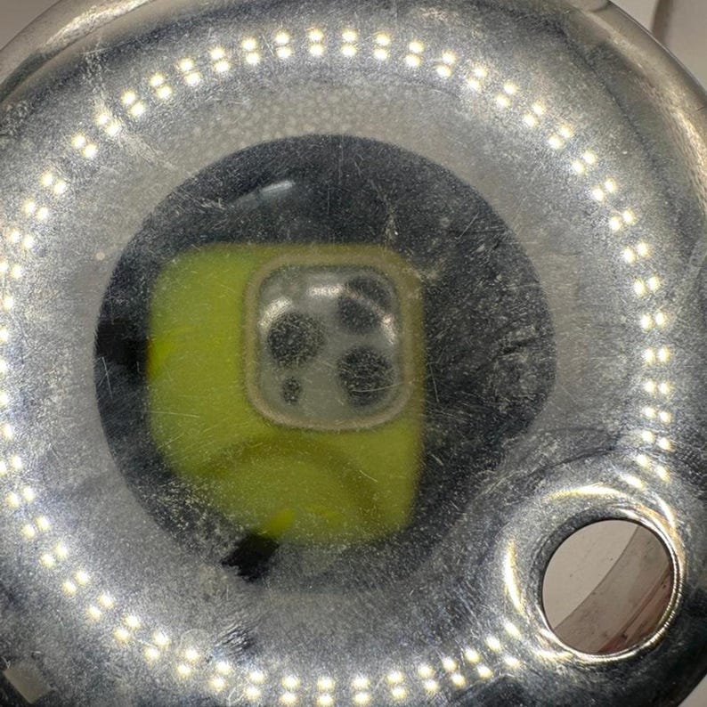 Pode incluir: Uma foto em close-up de uma luz de anel prateada com um telefone amarelo no centro. A luz do anel tem muitas pequenas luzes brancas ao redor da borda. O telefone tem uma protuber&acirc;ncia da c&acirc;mera.