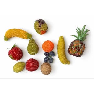Pode incluir: Uma variedade de decorações de frutas com contas, incluindo uma banana amarela, um morango vermelho, uma pera verde e um abacaxi com folhas verdes. A fruta é disposta sobre uma superfície branca.