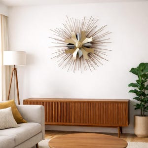 May include: A mid-century modern living room featuring a large, starburst-style wall art piece with gold, silver, and black accents. Below is a wooden cabinet with vertical grooves, a light-colored sofa, and a round coffee table.