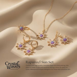 May include: A gold-toned jewelry set featuring a sunburst design with a purple center stone. The set includes a necklace, earrings, a ring, and hoop earrings, all displayed on a cream-colored fabric. The jewelry is from Crystal Waves.