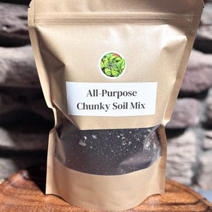 May include: A brown paper bag with a clear window, filled with dark chunky soil mix. The bag has a white label that reads "All-Purpose Chunky Soil Mix." A round sticker with green leaves is on the bag.