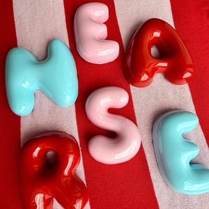 unsere leichten bubble Buchstaben im Keramik Look. sie glänzen um die Wette vor einem rot weißen Hintergrund