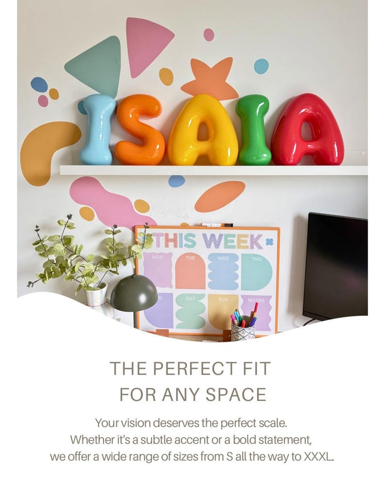 May include: Five glossy, rounded, three-dimensional letters spelling ISAIA in light blue, orange, yellow, green, and red. The letters are arranged on a white shelf against a wall decorated with colorful abstract shapes and a weekly planner board.