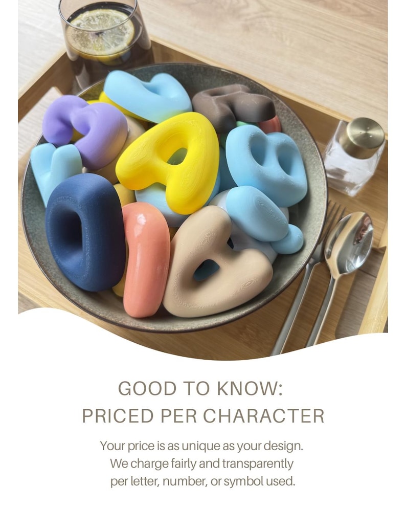 May include: A collection of smooth, matte-finish alphabet letters in various pastel and bold colors, including yellow, blue, pink, purple, and dark brown, contained within a dark gray bowl. The text GOOD TO KNOW: PRICED PER CHARACTER is visible.
