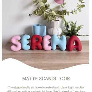 May include: A set of six individual 3D letters spelling the name SERENA, featuring a smooth matte finish. The letters are colored in a sequence of light pink, light blue, red, light pink, light blue, and red, arranged in a horizontal line.