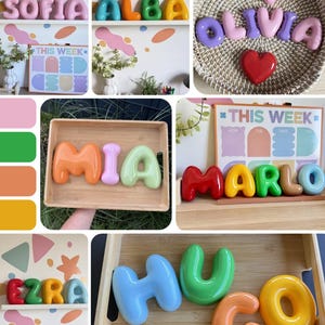 May include: A collection of glossy, three-dimensional, bubble-style letters in various bright colors, used to spell names like Sofia, Alba, Olivia, Mia, Marlo, Ezra, and Hugo. These smooth, rounded decorative letters are displayed on shelves, in wooden trays, or in woven baskets.