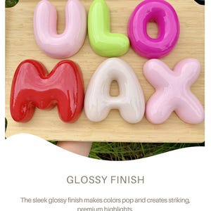 May include: A set of six three-dimensional, glossy, bubble-style letters spelling ULO MAX. The letters are arranged in two rows on a light wood surface. The colors include light pink, lime green, magenta, bright red, cream, and pale pink.