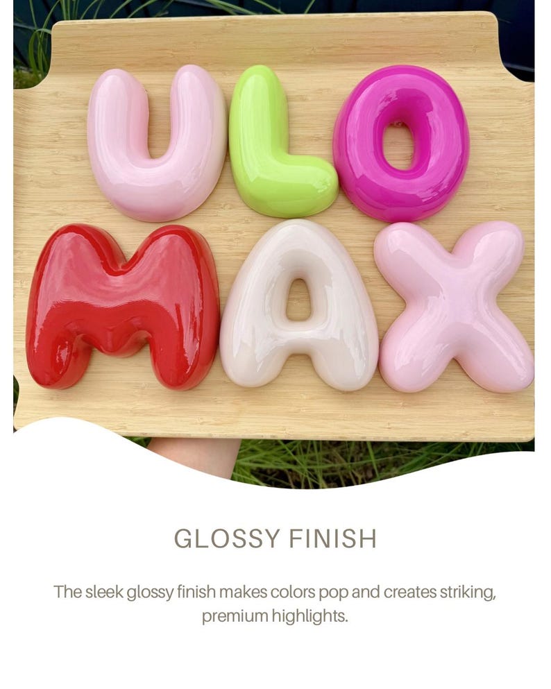 May include: A set of six three-dimensional, glossy, bubble-style letters spelling ULO MAX. The letters are arranged in two rows on a light wood surface. The colors include light pink, lime green, magenta, bright red, cream, and pale pink.