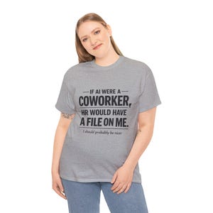 Op de afbeelding: Een lichtgrijs t-shirt met de zwarte tekst "-IF AI WERE A- COWORKER, HR WOULD HAVE A FILE ON ME. I should probably be nicer". Het t-shirt wordt door een persoon gedragen.