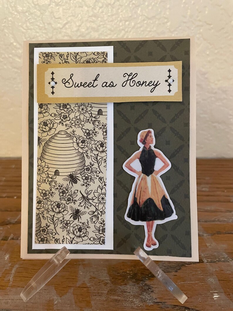 Puede incluir: Tarjeta de felicitaci&oacute;n hecha a mano con un dise&ntilde;o floral y de abejas. La tarjeta presenta una pancarta decorativa que dice "Sweet as Honey". Una pegatina de una mujer con un vestido vintage est&aacute; en el lado derecho.