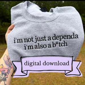May include: A light gray crewneck sweatshirt featuring black embroidered text that reads, "i'm not just a dependa i'm also a b*tch." A light purple banner graphic is overlaid at the bottom with the black text "digital download" inside.