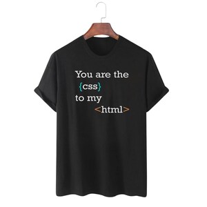 May include: A black short-sleeved t-shirt featuring the white text "You are the" followed by "{css}" in teal, "to my" in white, and "<html>" in orange. The shirt has a crew neckline and is displayed on a wooden hanger against a plain background.