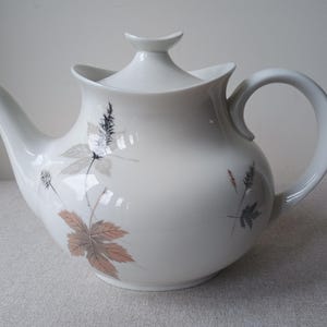 Peut inclure: Une tasse en céramique blanche avec une anse noire et le texte "But First, Coffee" en gras noir. La tasse est posée sur un fond flou, suggérant un cadre chaleureux.