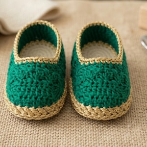 May include: A pair of handmade baby booties. The booties are a vibrant green with a gold-coloured trim around the opening and base. The crochet stitch creates a textured appearance. The booties are designed for infants.