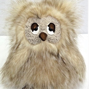 May include: A plush owl toy with a fluffy, light brown fur exterior. The owl has large, round eyes with dark brown pupils and a small, brown beak. The toy is designed to resemble a real owl.