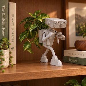 May include: A light grey, speckled robot-shaped planter with a rectangular head, two circular eyes, and articulated limbs. The robot carries a backpack-style container holding a green and yellow variegated pothos plant, standing upright.