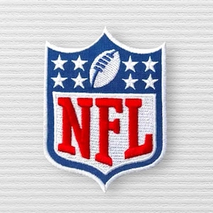 May include: Embroidered NFL shield patch featuring a blue border with white stars and a football. The letters "NFL" are in red with a white outline. The patch is on a white textured background.