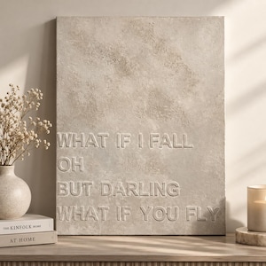 May include: A rectangular beige wall art piece with a textured, stone-like surface. The text WHAT IF I FALL OH BUT DARLING WHAT IF YOU FLY is embossed in capital letters across the centre of the piece, matching the beige colour of the background.
