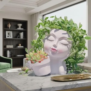 May include: A white face planter with closed eyes and a gentle smile, holding a small white pot with a succulent. The planter is adorned with green leafy vines, creating a unique and artistic display. A gold tray with scissors is on the table.