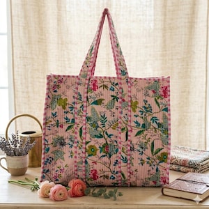 May include: A pink floral tote bag with matching handles. The bag features a repeating pattern of flowers and leaves in shades of green, blue, and red. The bag is made of quilted fabric.