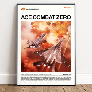 May include: A framed poster for the video game "Ace Combat Zero" featuring two fighter jets against a fiery explosion backdrop. The poster has the game's title and the Bandai Namco logo at the top.