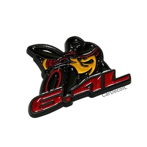 Puede incluir: Un emblema de metal que presenta un personaje de abeja negro estilizado con detalles en amarillo, colocado sobre el texto 6.4L en rojo y negro. El diseño tiene un acabado brillante con bordes elevados y una estética distintiva de insignia.