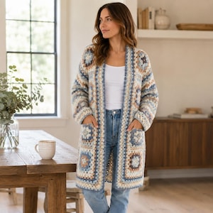 May include: A long, open-front crochet cardigan in a patchwork design. The color palette includes shades of blue, beige, and brown. The cardigan has two front pockets and is worn over a white top and blue jeans.