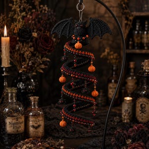 May include: A hanging crochet ornament featuring a black bat with red eyes at the top, connected to a spiraling black and red structure. The spiral is decorated with small orange crocheted pumpkins, dark beads, and tiny black spider charms.
