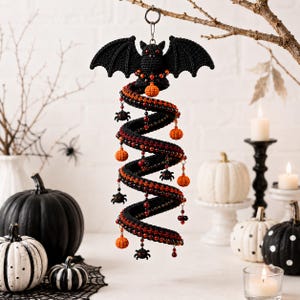 May include: A hanging crochet decoration featuring a black bat at the top, connected to a long, spiraling black and orange tube. The spiral is adorned with small orange crochet pumpkins, black crochet spiders, and red beads hanging from thin chains.