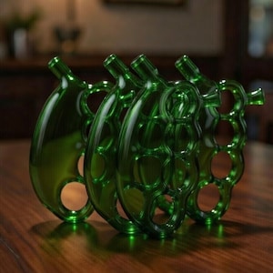 May include: Four green glass decorative bottles with a unique design, each featuring a bulbous body and a slender neck. The bottles have a series of circular cutouts and are arranged on a dark wooden surface, reflecting the ambient light.