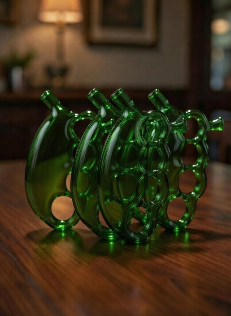 May include: Four green glass decorative bottles with a unique design, each featuring a bulbous body and a slender neck. The bottles have a series of circular cutouts and are arranged on a dark wooden surface, reflecting the ambient light.
