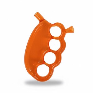 May include: An orange glass pipe with a brass knuckle design. The pipe features four finger holes and two angled mouthpieces. The glass is a translucent orange color, and the overall shape is ergonomic.