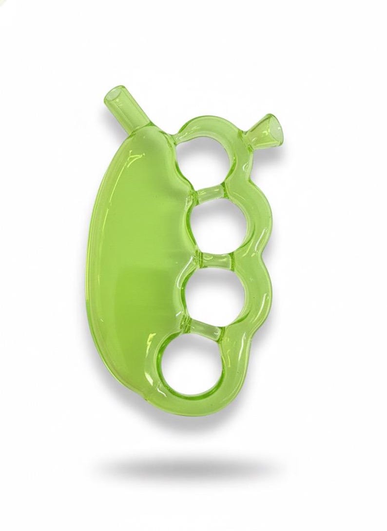 May include: A transparent, lime green glass pipe with a unique design. The pipe features a rounded, oblong bowl connected to a series of three finger-sized rings, and a mouthpiece. The overall shape resembles a set of brass knuckles.