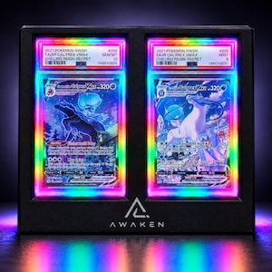 May include: A black display frame with the AWAKEN logo containing two PSA-graded 2021 Pokemon SWSH Chilling Reign trading cards. The cards feature Shadow Rider Calyrex VMAX and Ice Rider Calyrex VMAX, illuminated by a vibrant rainbow LED light border.